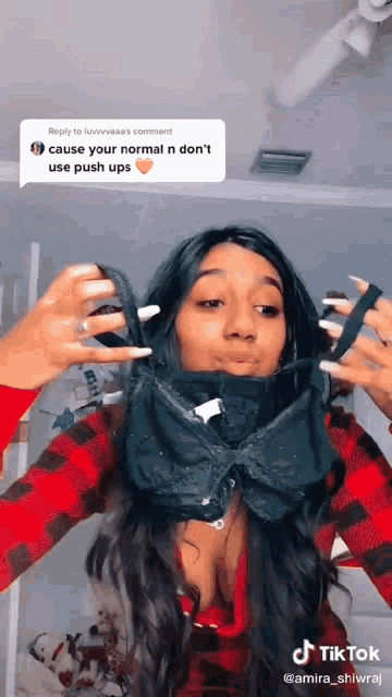 a woman wearing a plaid shirt is holding a bra in front of her face .