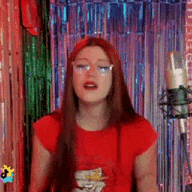 a woman in a red shirt is singing into a microphone in front of a curtain .