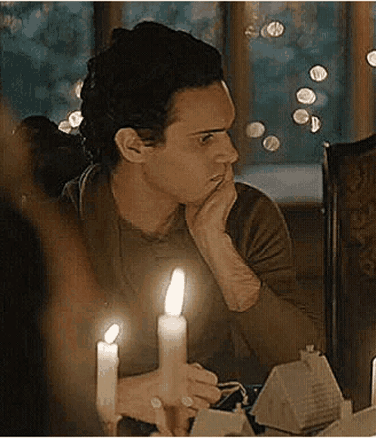 a man is sitting at a table with candles lit and looking at something .