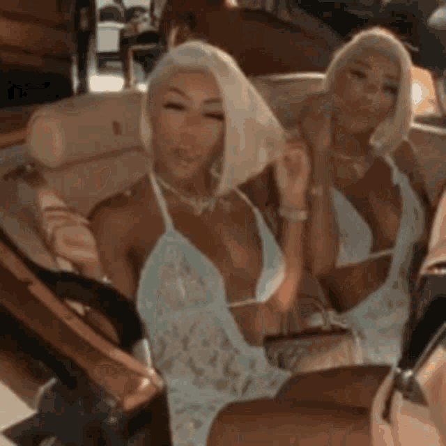 two women are sitting next to each other in a car wearing bikinis .