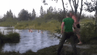 a man in a green shirt is standing next to a river with people swimming in it