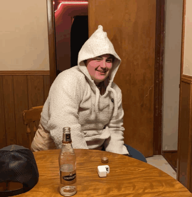 a man wearing a white hoodie sits at a table with a bottle of crown royal on it