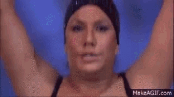 a woman is jumping into a pool with a crowd watching .