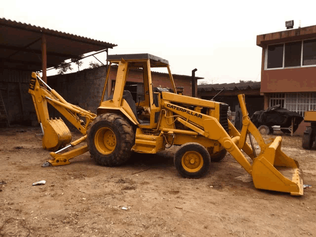 a yellow caterpillar backhoe is parked in the dirt