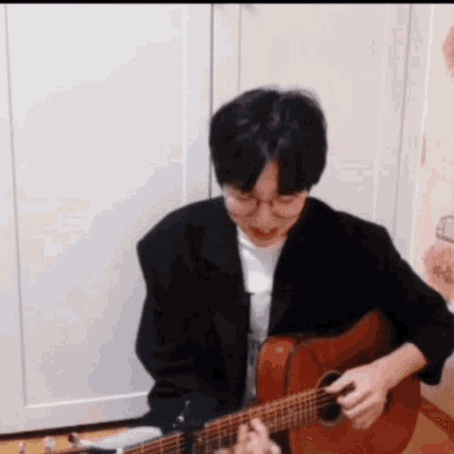 a man in a black jacket is playing an acoustic guitar .