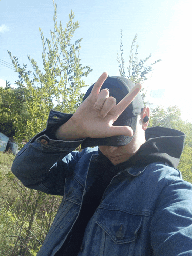 a man wearing a denim jacket and a black hat makes a peace sign