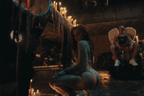 a woman in a bikini is squatting in front of candles and a man with angel wings
