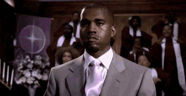 a man in a suit and pink tie is standing in front of a choir .