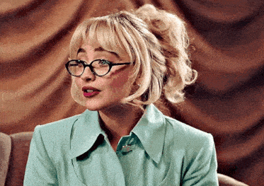 a woman wearing glasses and a blue jacket is sitting on a chair .