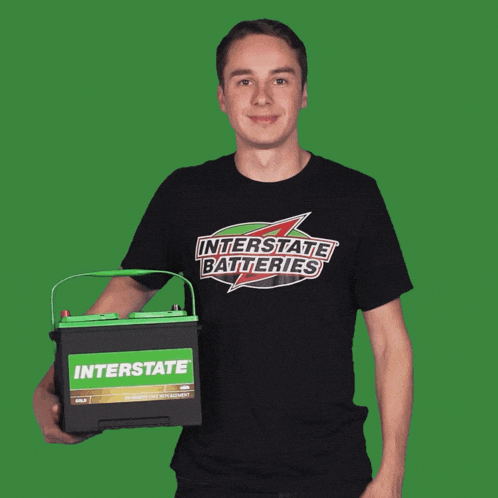 a man wearing an interstate batteries shirt is holding a battery and giving a thumbs up