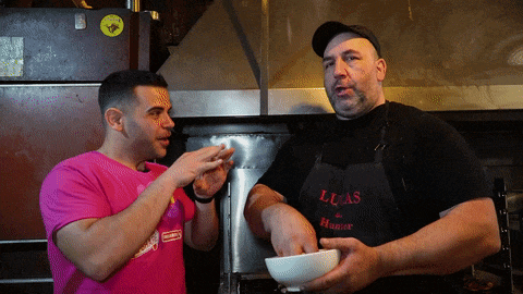 a man wearing an apron that says lucas on it is talking to another man