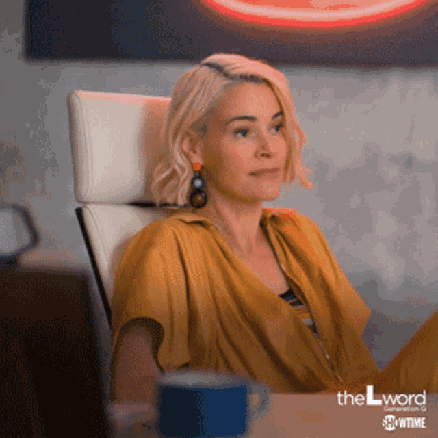 a woman in a yellow shirt is sitting in a chair in front of a neon sign that says the l word