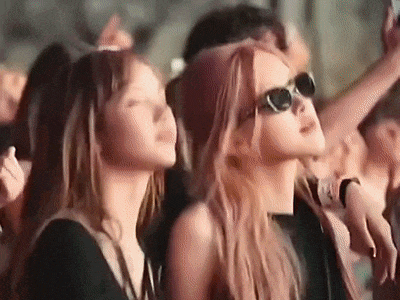 a group of people are sitting in a crowd at a concert . one of the women is wearing sunglasses .