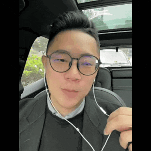 a man wearing glasses and ear buds is sitting in a car