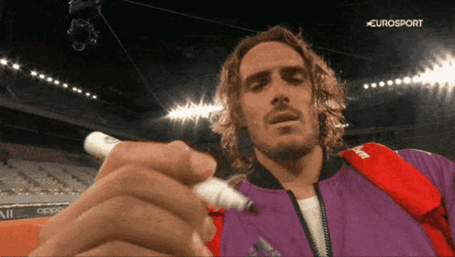 a man in a purple jacket is writing with a marker in front of a eurosport logo