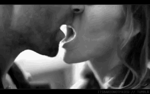 a black and white photo of a man and woman kissing with their mouths open .