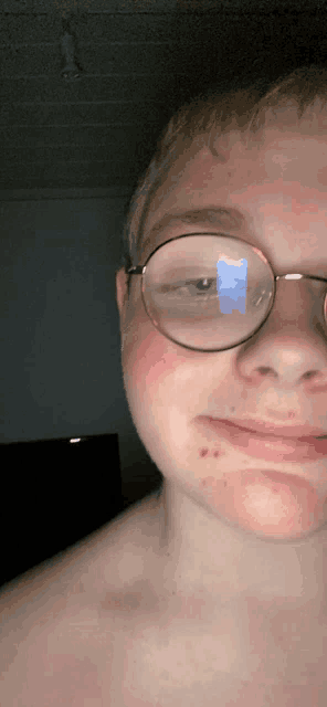 a boy wearing glasses has a reflection of a blue object in his eye