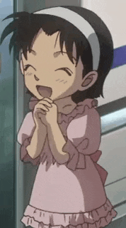 a little girl in a pink dress is standing next to a wall with her hands folded .