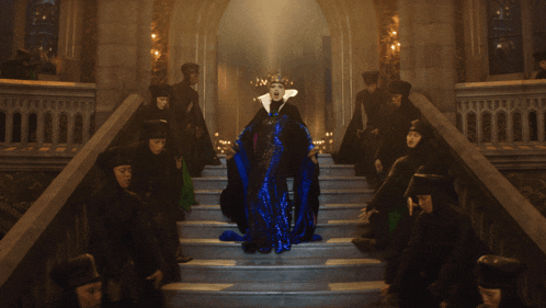 a woman in a blue cape with a crown on her head is surrounded by other people