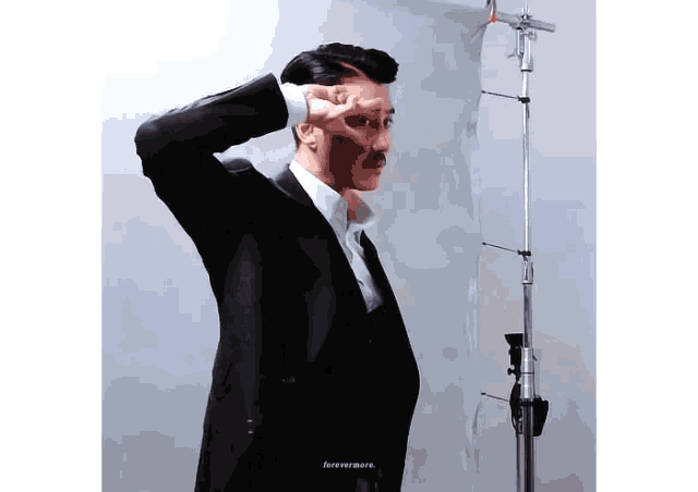 a man in a suit with a mustache is standing in front of a microphone .