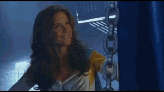 a woman in a white dress is standing in front of a blue curtain with chains .