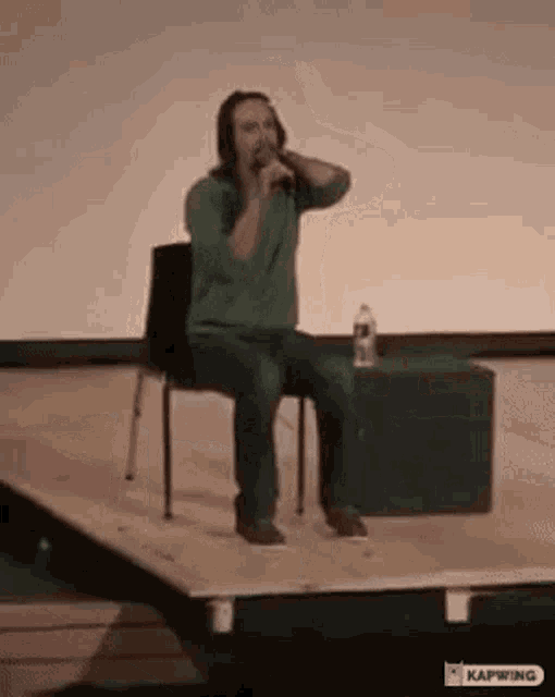 a man is sitting on a stage holding a microphone .