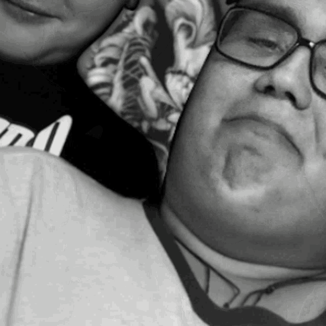 a man wearing glasses is laying next to a woman wearing a black shirt that says m1