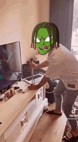 a man with dreadlocks is standing in front of a laptop and a tv .
