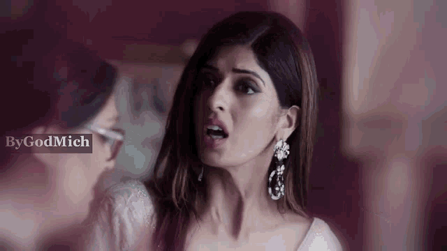 a woman wearing earrings is making a funny face while standing next to another woman .