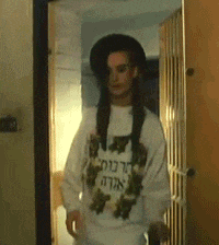 a woman wearing a white sweater with flowers on it is standing in a doorway