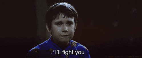 a young boy in a blue shirt is holding his fist in the air and saying `` i 'll fight you '' .