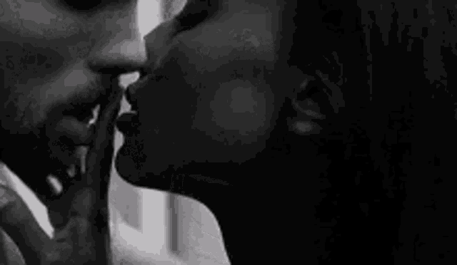 a black and white photo of a man kissing a woman on the neck .
