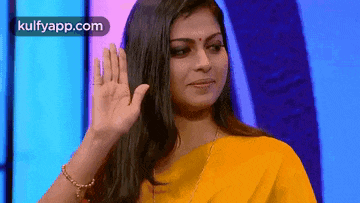 the woman is wearing a yellow saree and waving her hand .