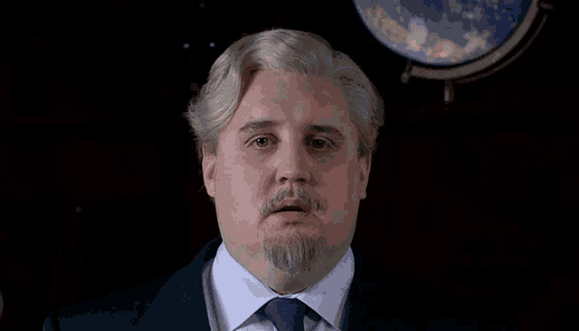 a man with gray hair and a beard is pointing at the camera