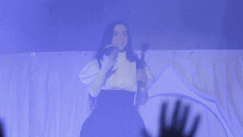 a woman singing into a microphone with her hands raised in the air
