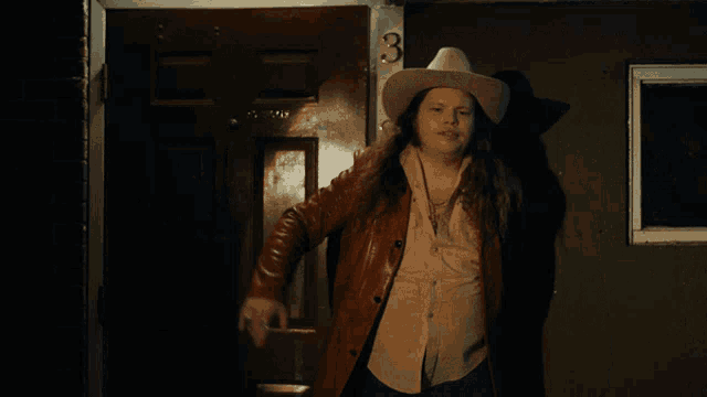 a man in a cowboy hat is standing in front of a door that has the number 3 on it