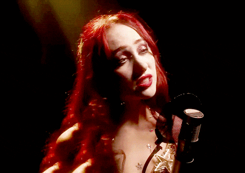 a woman with red hair singing into a microphone in a dark room