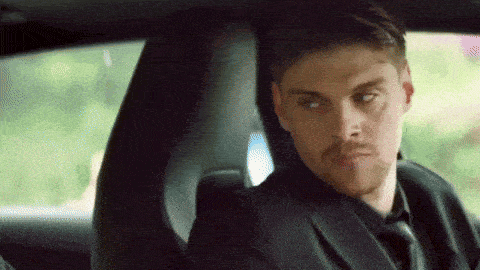 a man in a suit and tie is sitting in the driver 's seat of a car looking at the camera .