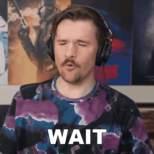 a man wearing headphones and a purple tie dye shirt says wait