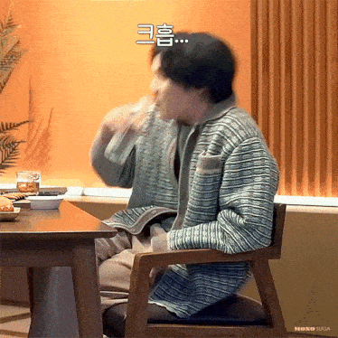 a man in a striped shirt is sitting at a table drinking from a bottle