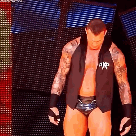 a shirtless wrestler is walking on a stage in front of a screen .