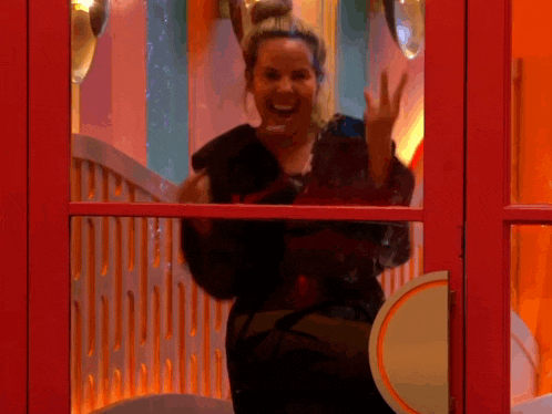 a woman is standing in front of a red door waving