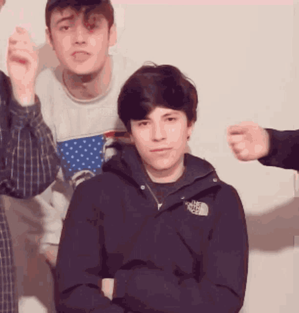 a young man wearing a north face jacket stands with his arms crossed in front of two other young men