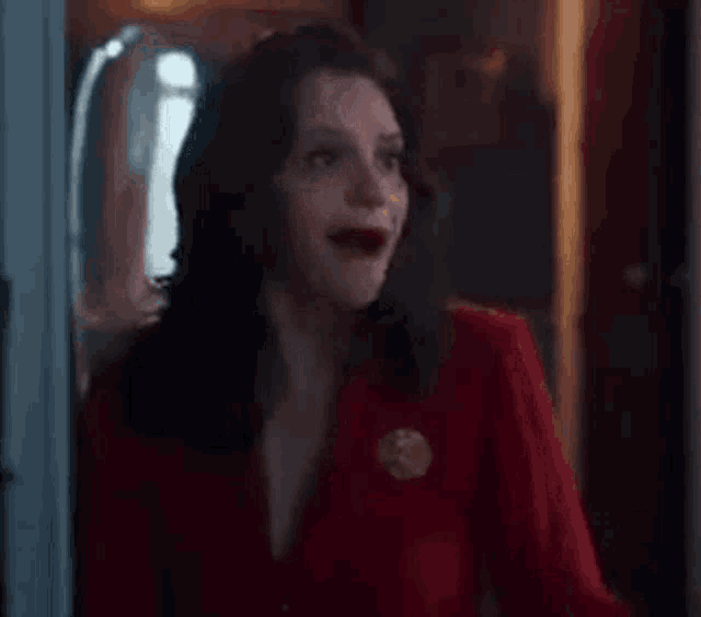 a woman in a red shirt is standing in front of a door with her mouth open .