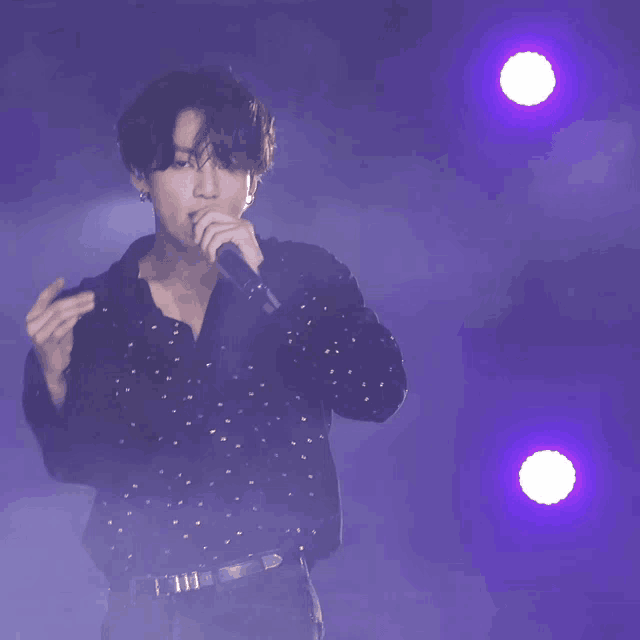 a man singing into a microphone with a purple background