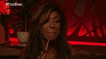 a woman is smoking a cigarette in a dark room with a red background .