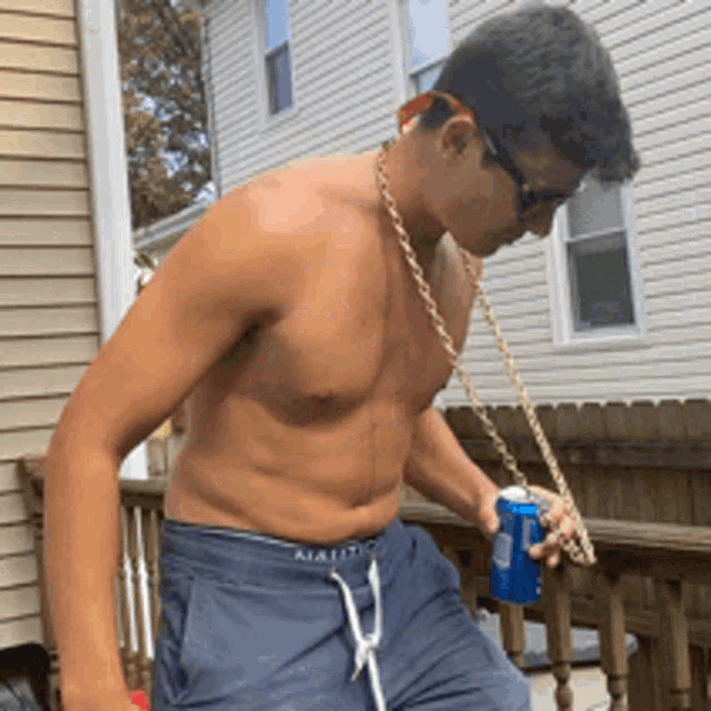 a shirtless man wearing sunglasses and a chain around his neck is holding a can of soda
