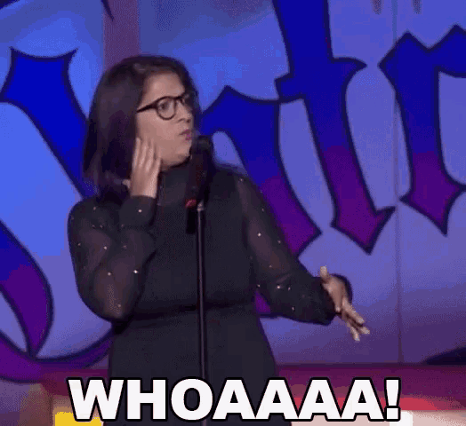 a woman wearing glasses stands in front of a microphone and says whoaaa !