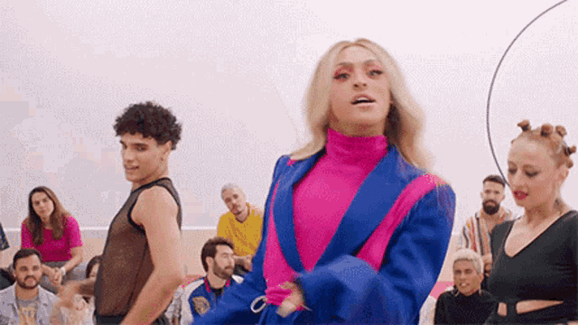 a group of people are dancing in a room with a woman in a pink and blue jacket .