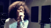 a woman with an afro is singing into a microphone in a dark room .